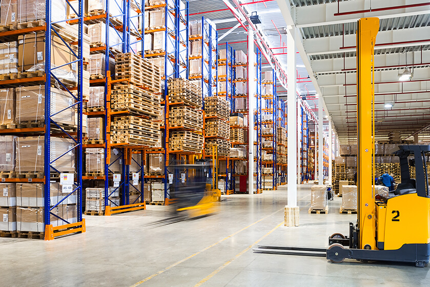 Spacious warehouse with tall shelves of boxes and a yellow forklift moving in foreground.