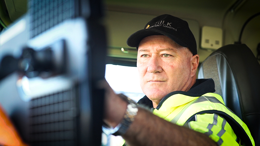 Man in high-vis jacket operates machinery inside vehicle, focused on tasks.