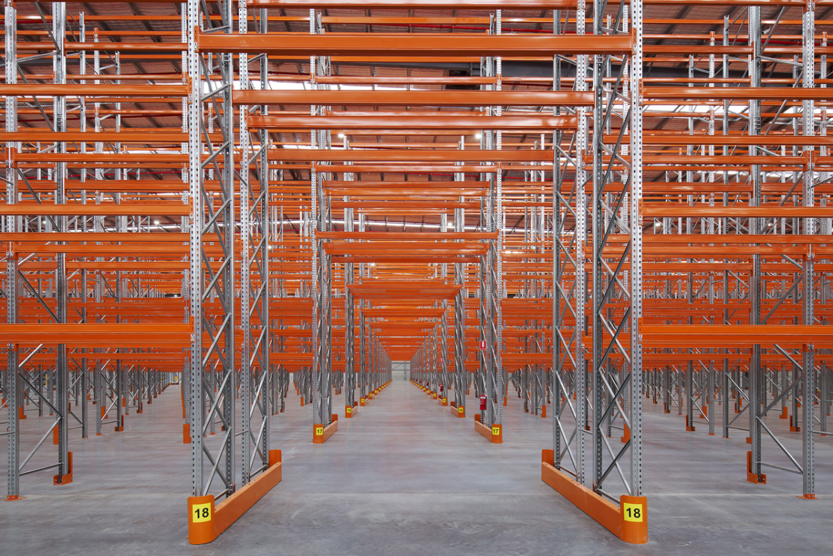 Spacious warehouse with tall shelves, orange beams, metal supports, and clear concrete floor.